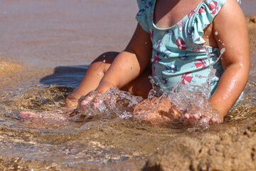 Little baby on the beach playing in the sea water. Small child in colorful swimsuit with hands in water