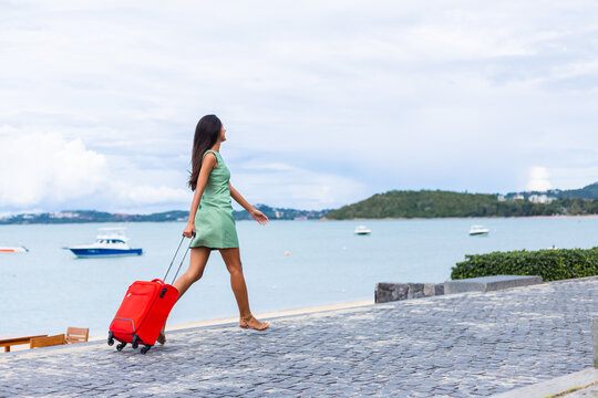 Young happy beautiful woman in dress with red suitcase on vacation by tropical beach 