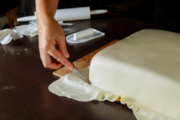 Chef cutting white fondant on square cake.