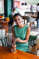 Cute elegant calm happy woman in green summer dress sits with coffee in cafe enjoying morning. Beautiful coffee lover. 