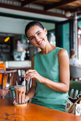 Cute elegant calm happy woman in green summer dress sits with coffee in cafe enjoying morning. Beautiful coffee lover. 