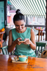 Tanned pretty woman smiling and take photo of coffee in cafe  