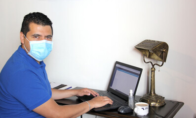 Fototapeta na wymiar latin man with protection mask and antibacterial gel, working in home office and drinking coffee, new normal