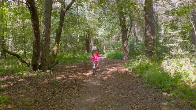 Little girl on bicycle in forest driving tracking forward camera movement