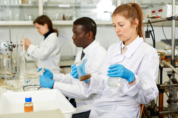 Fototapeta premium Focused women lab technicians in glasses working with reagents and test tubes, man on background