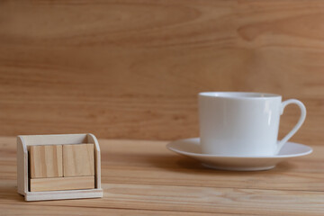 Empty wooden calendar blocks for insert date time with blurred white coffee cup or teacup on pinewoods table and brown wooden wall background.