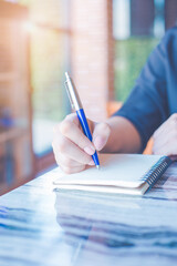 Woman is writing on a notebook with a pen in the office.