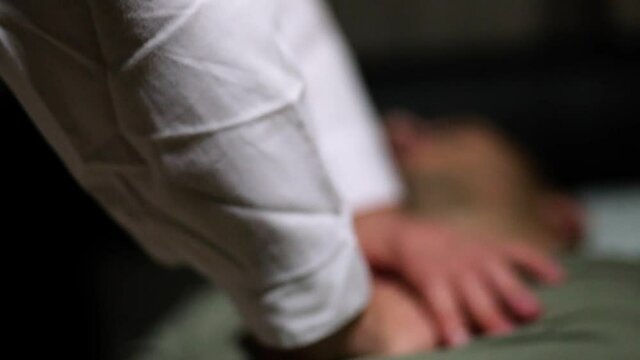 Close-up hands of a doctor doing artificial respiration. A man lies on a medical cart. The focus of the camera moves back and forth. The room is dimmed light.