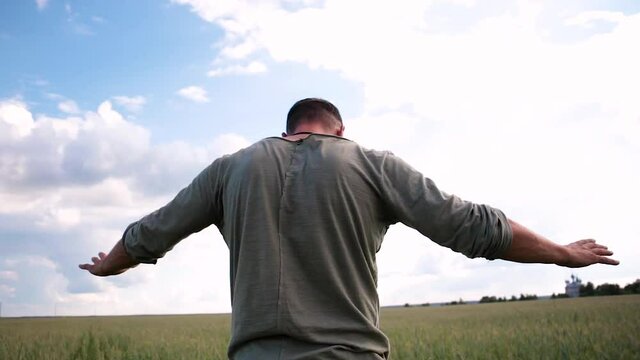 A young man is standing in the field, saying something. He spreads his arms in different directions, points forward. The camera moves around the person. Against the background of the blue sky.