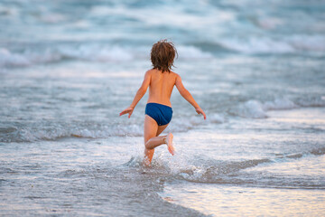 Happy child running in the sea. Kid boy having fun on the beach. Summer vacation and healthy kids.
