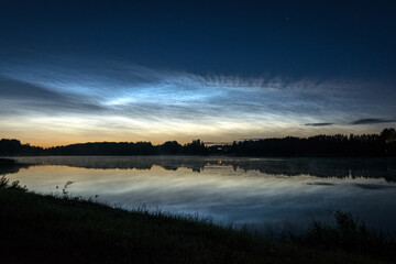 night landscape with white silver clouds over the lake, blurred foreground, charming cloud reflections in the lake water, summer night