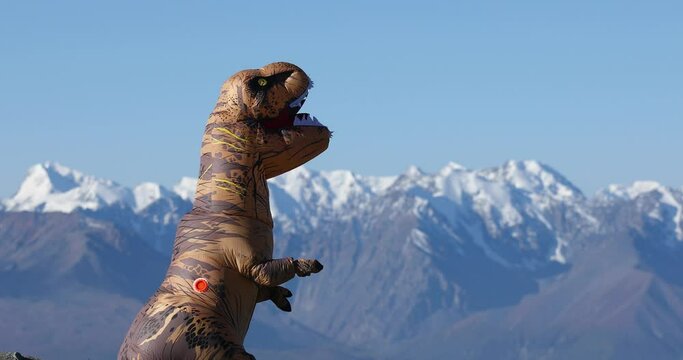 Tyrannosaurus Rex dinosaur. Big dinosaur doll with person inside walking in mountains in sunny summer day. Inflatable doll. Beautiful installation outdoors on nature with prehistoric animal.