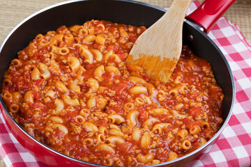Goulash and noddles in a red skillet with wooden spatula