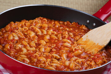 Goulash and noddles in a red skillet with wooden spatula