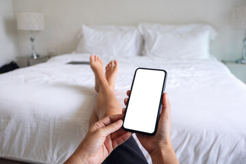 Mockup image of a woman holding and using mobile phone with blank screen while relaxing and lying on the bed