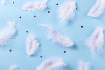 White feather and sIlver confetti on blue background. Soft delicate texture. Stylish luxury pattern. Flat lay, top view