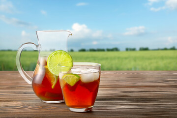Glass and jug of tasty cold ice tea on table outdoors