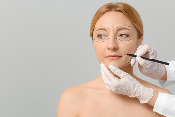 Plastic surgeon applying marks on woman's face against grey background