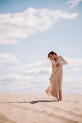 Young, slender girl in beige dress walks in the desert