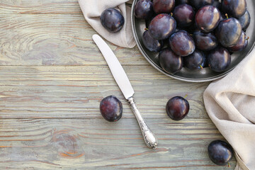 Plate with ripe plums and knife on wooden background