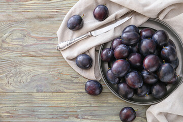 Plate with ripe plums and knife on wooden background