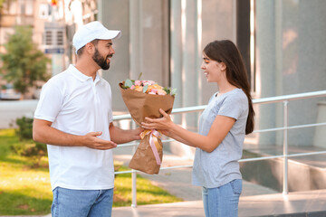 Young woman receiving bouquet of flowers from courier outdoors