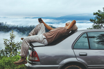 Men relax on car roof and holding coffee cup at mountain covered in foggy during morning sunrise.