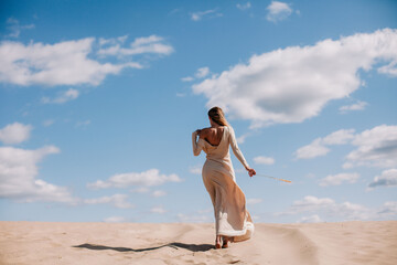 Young, slender girl in beige dress walks in the desert