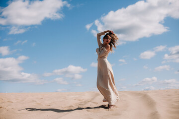 Young, slender girl in beige dress walks in the desert