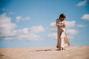 Young, slender girl in beige dress walks in the desert