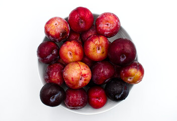 Fresh plums in a bowl, isolated on white background. Top view
