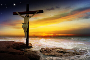 Crucifix crucifixion Jesus Christ on the rocks by the sea at sunset.