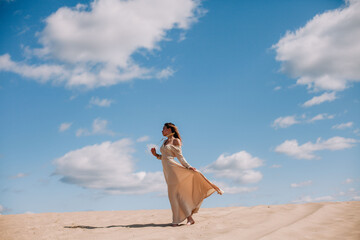 Young, slender girl in beige dress walks in the desert