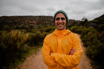 Smiling young male athlete crossed arms resting after sprinting on wet gravel mountain path on cloudy cold day