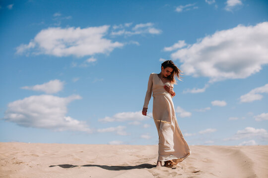 Young, slender girl in beige dress walks in the desert