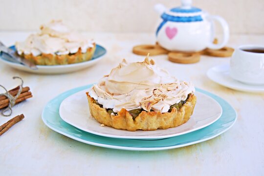 Mini tarts with custard, gooseberries and meringue on a white plate on a light concrete background. Desserts meringue.