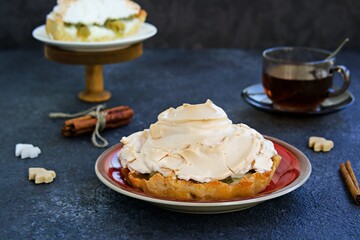 Mini tarts with custard, gooseberries and meringue on a white plate on a dark concrete background. Desserts meringue.