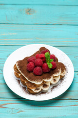 portion of Classic tiramisu dessert with raspberries on blue wooden background