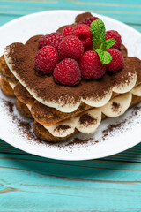 portion of Classic tiramisu dessert with raspberries on blue wooden background
