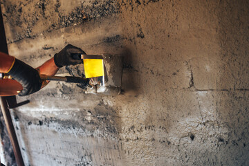 Man plastering a wall with mortar using a hopper bucket.