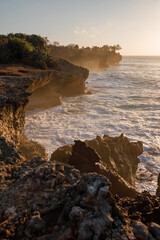 Vertical shot sunset seascape with rocky beach and crashing waves