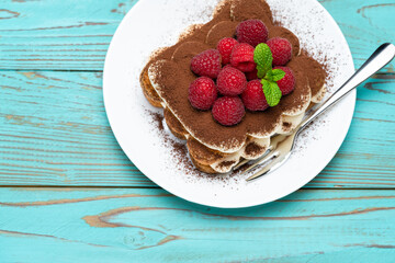 portion of Classic tiramisu dessert with raspberries on blue wooden background