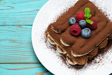 portion of Classic tiramisu dessert with raspberries and blueberries on blue wooden background