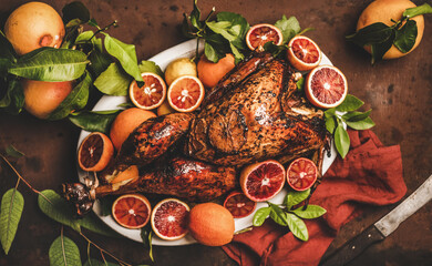 Christmas or Thanksgiving Day festive table setting. Whole roasted turkey with citrus fruit over rusty table background, top view, selective focus. Holiday gathering food concept
