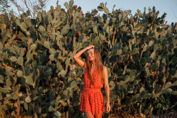 Young tourist woman standing near a big opuntia cactusm smiling ad touch the hair. Summer tropical vacation concept