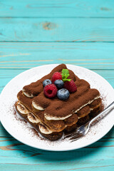 portion of Classic tiramisu dessert with raspberries and blueberries on blue wooden background