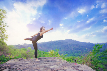 Young woman standing and doing yoga pose at the top of mountain in the morning	