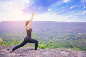 Young woman standing and doing yoga pose at the top of mountain in the morning	