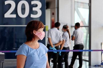 Fototapeta na wymiar Woman in protective face mask in the airport terminal. Passenger are waiting for their flight, safety measures during the covid-19 coronavirus pandemic