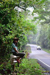 Obraz premium The girl sit on the barrier on the side of the road.